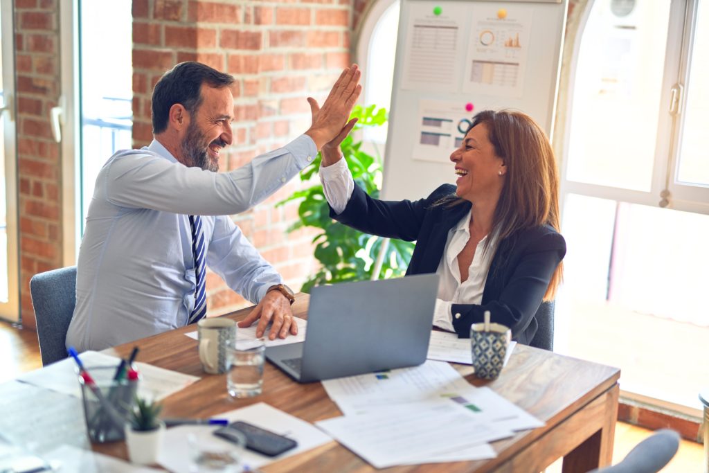 A man and a woman high five in front of a computer, at a desk