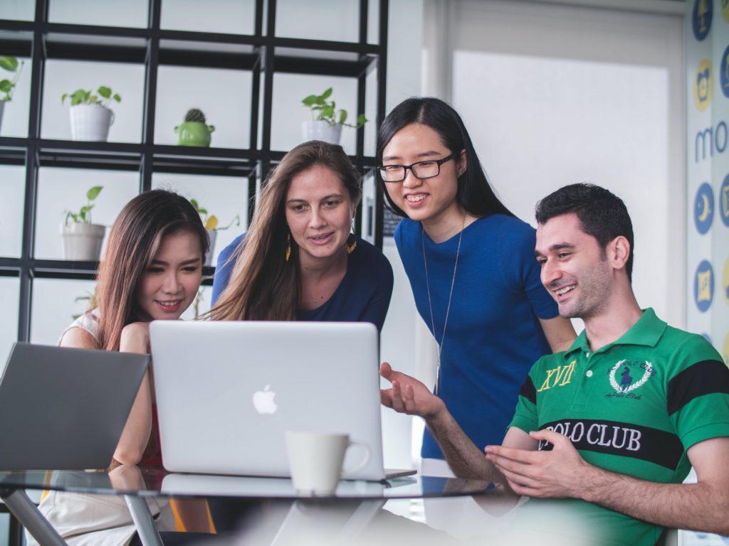 Four people stand around a computer sharing ideas